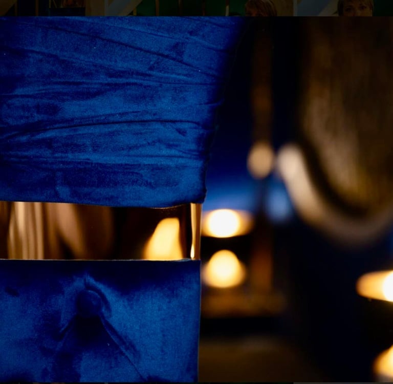Elegant blue velvet chair with a gold metallic band detail set in a dim room with glowing candles.