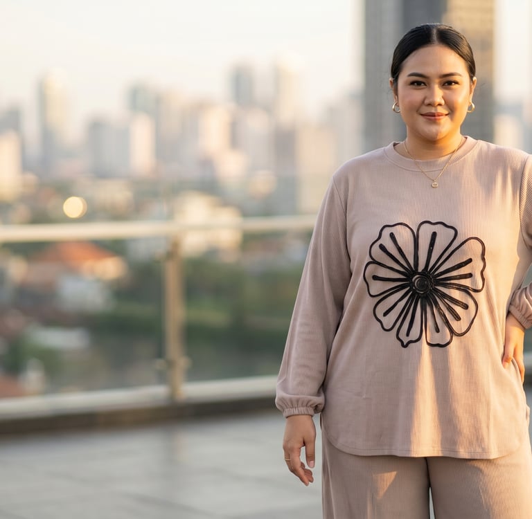 Plus-size woman in a beige floral sweatshirt posing on an urban rooftop with a city skyline view.