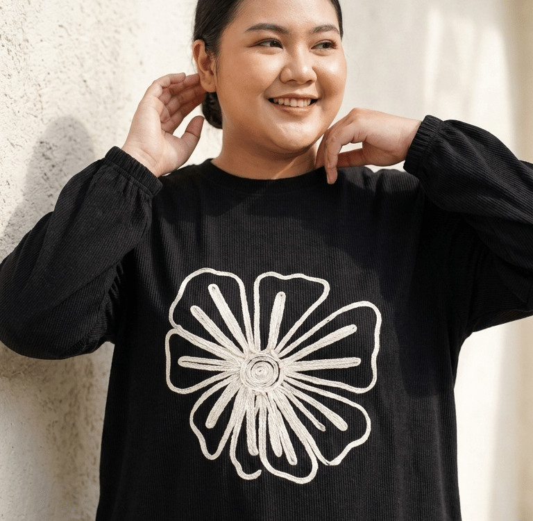 Smiling woman wearing a black long-sleeve sweatshirtwith a white floral embroidery.