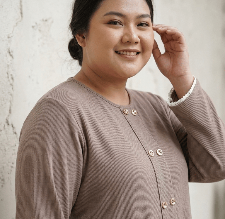 Smiling plus size woman wearing a brown ribbed double button blouse against a neutral wall.