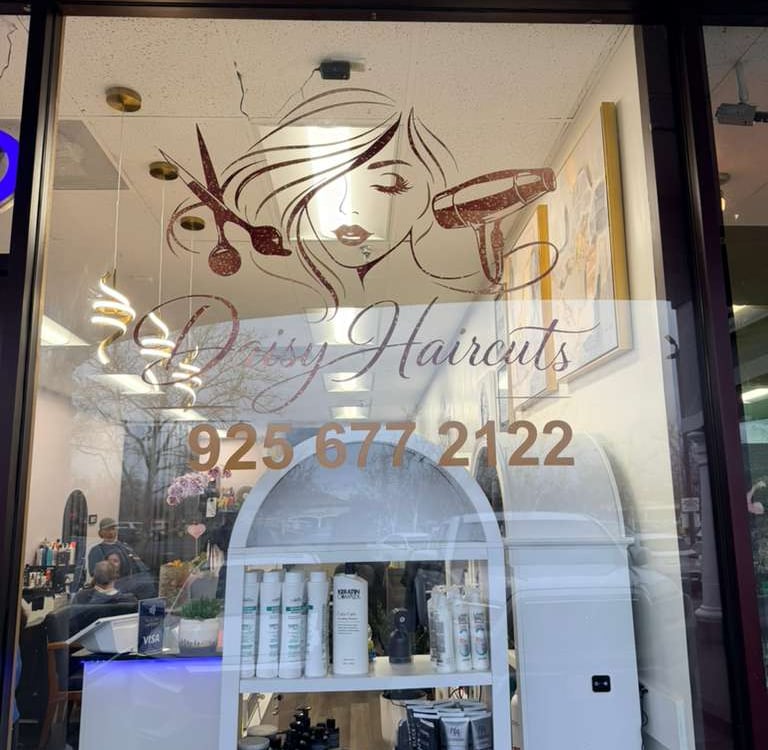 Drissy Haircuts storefront window with salon logo, contact number, and hair care products on display.