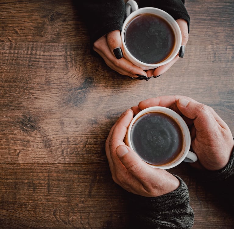 Two people holding cups of coffee meet to talk