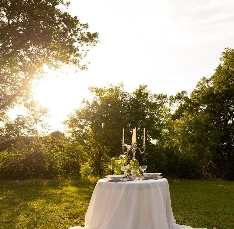 Elegant outdoor dinner table set with a white tablecloth and candelabra in a sunlit garden.