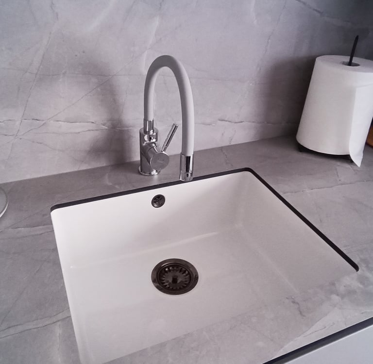 Modern white undermount kitchen sink with a sleek gooseneck faucet on a grey marble countertop.