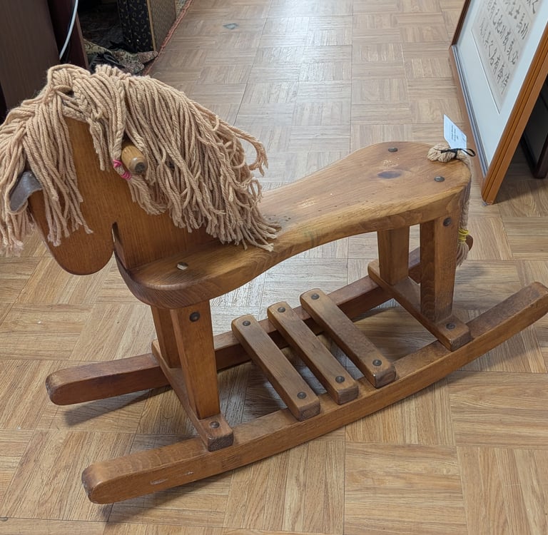 Vintage wooden rocking horse toy with yarn mane on a parquet floor.