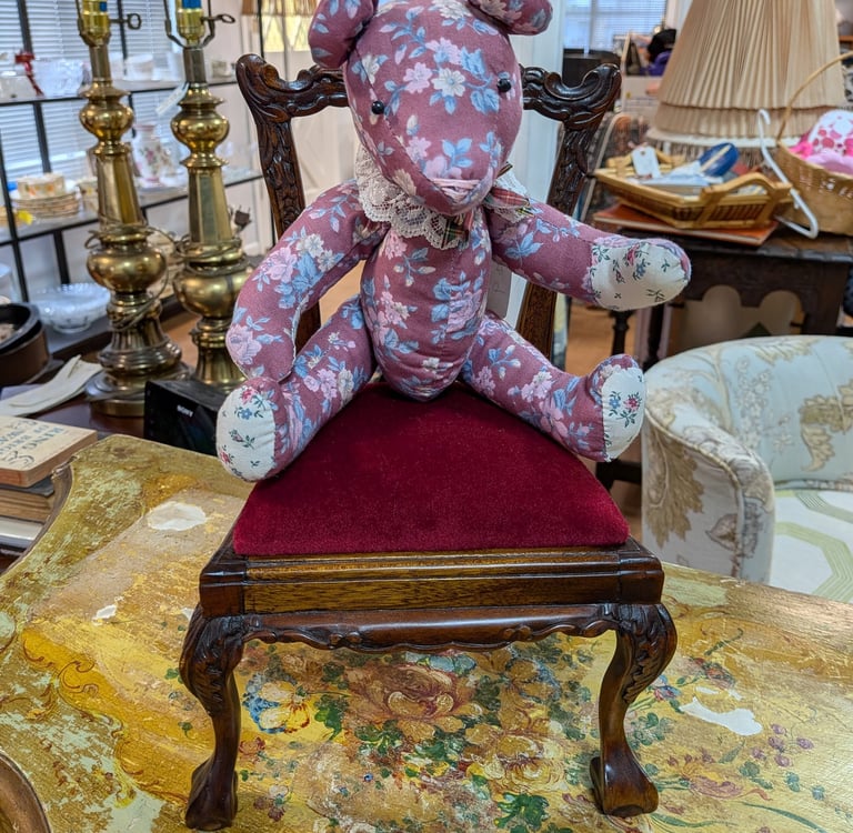 Vintage floral fabric teddy bear sitting on a miniature red velvet ornate wooden chair.