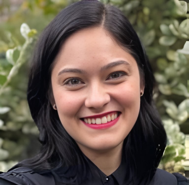Smiling woman with black hair and red lipstick posing against a blurred green garden background.