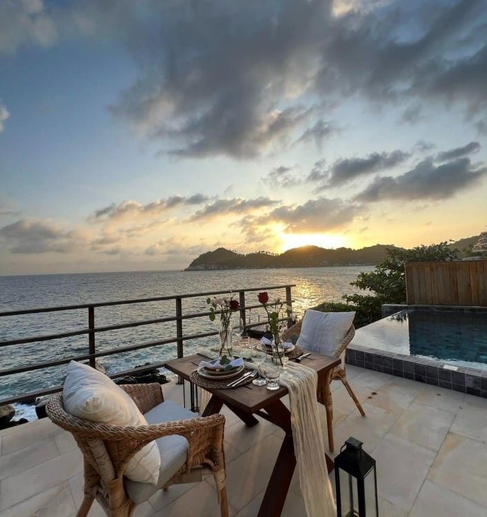 A romantic sunset dinner table set for two on a private oceanfront balcony with an infinity pool.
