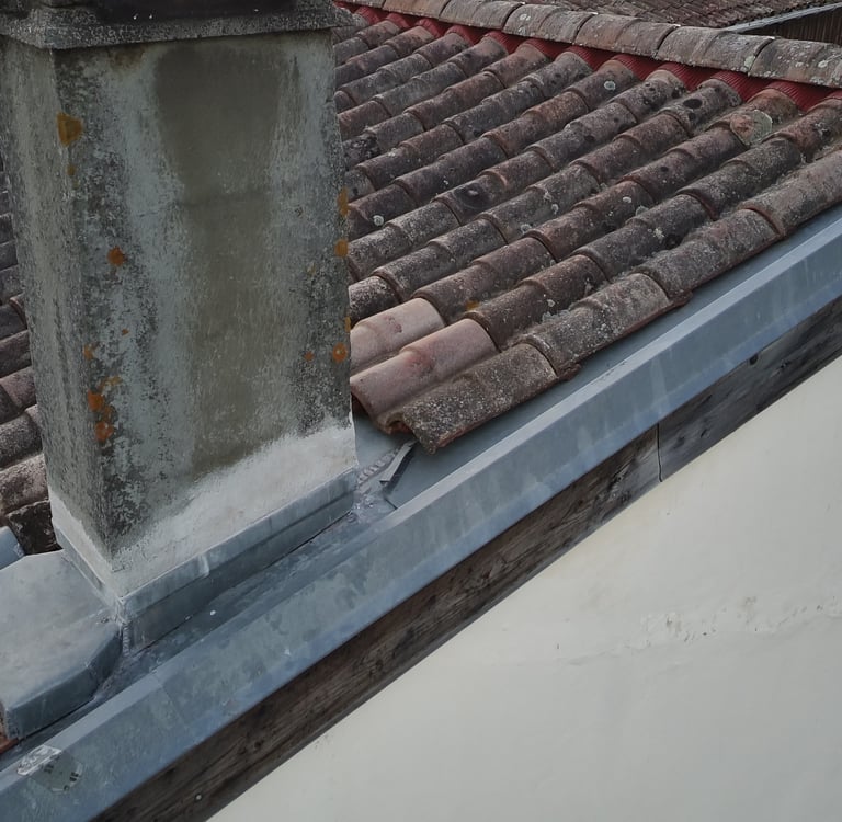 Installation de fléchage et gouttière en zinc sur un toit en tuile avec une cheminée en bêtonen 