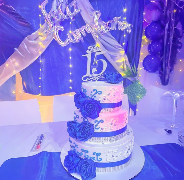 Elegante pastel de quinceañera de tres niveles con rosas azules y detalles plateados, con un adorno 