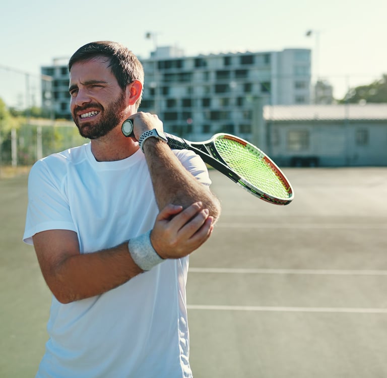 A male tennis player holding his painful elbow, demonstrating a common tennis elbow injury on court.
