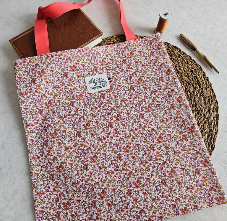 Handmade floral cotton tote bag with pink handles next to a journal, thread, and pen.