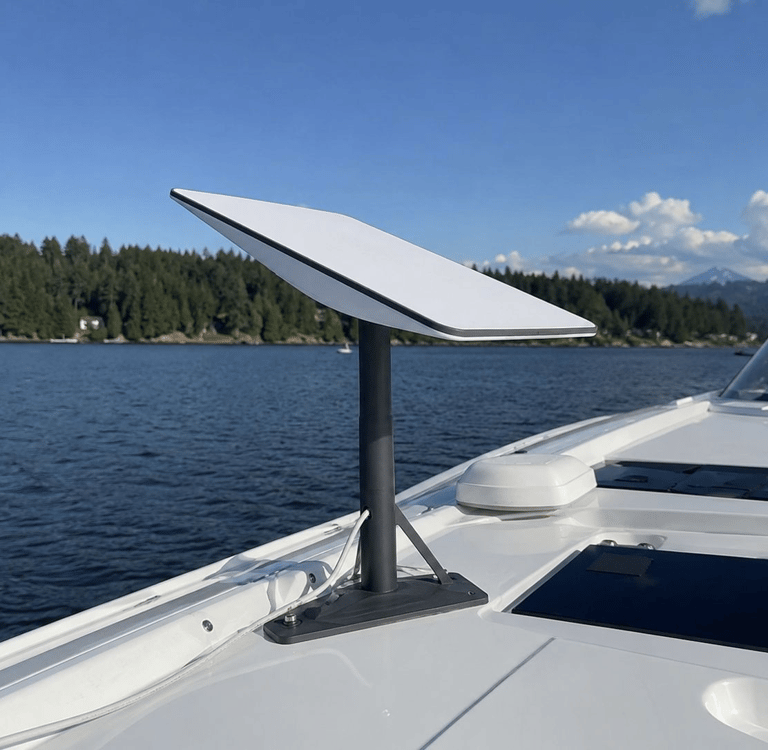 A Starlink satellite internet dish mounted on a white boat deck with a scenic lake background.