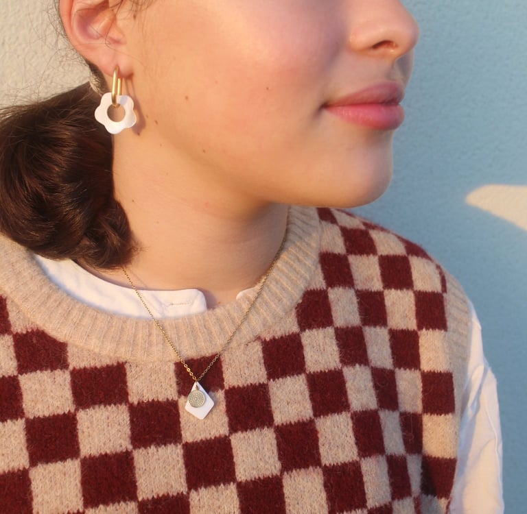 A young woman wearing white floral hoop earrings and a checkered sweater vest in golden hour light.