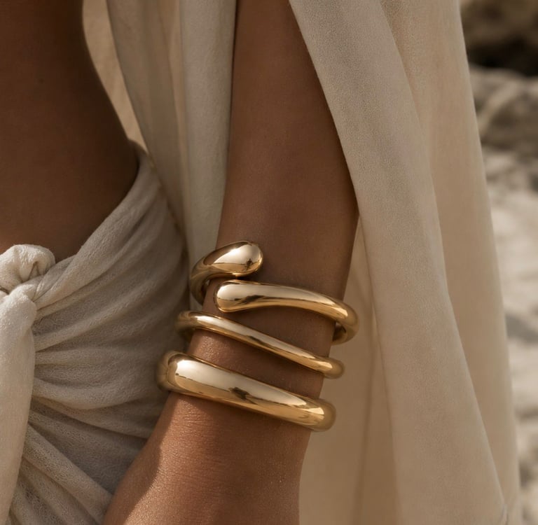 Gold statement bracelets styled on a wrist with a flowing beige beach cover-up.