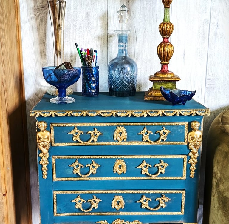 Antique blue and gold ornate dresser with a vintage orange lamp and dried flowers on top.
