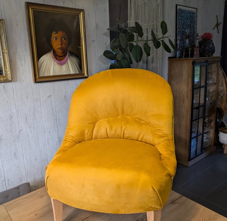 Yellow velvet accent chair with wooden legs in a stylish living room interior.