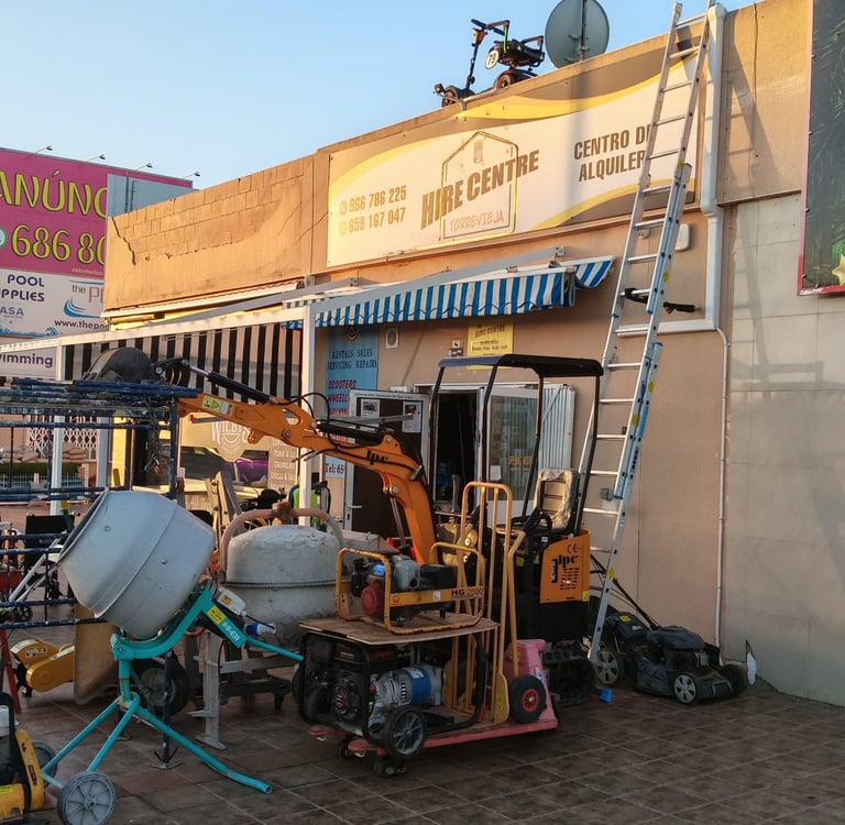 Concrete mixer and mini excavator parked outside a construction equipment hire centre storefront.