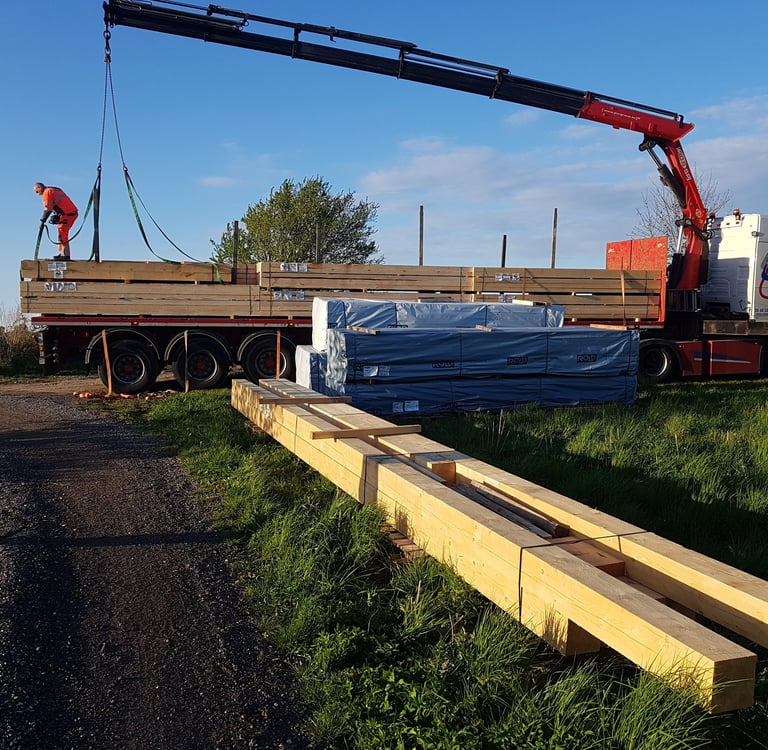 En kranlastbil aflæsser stakke af byggetræ og tømmer på en byggeplads.