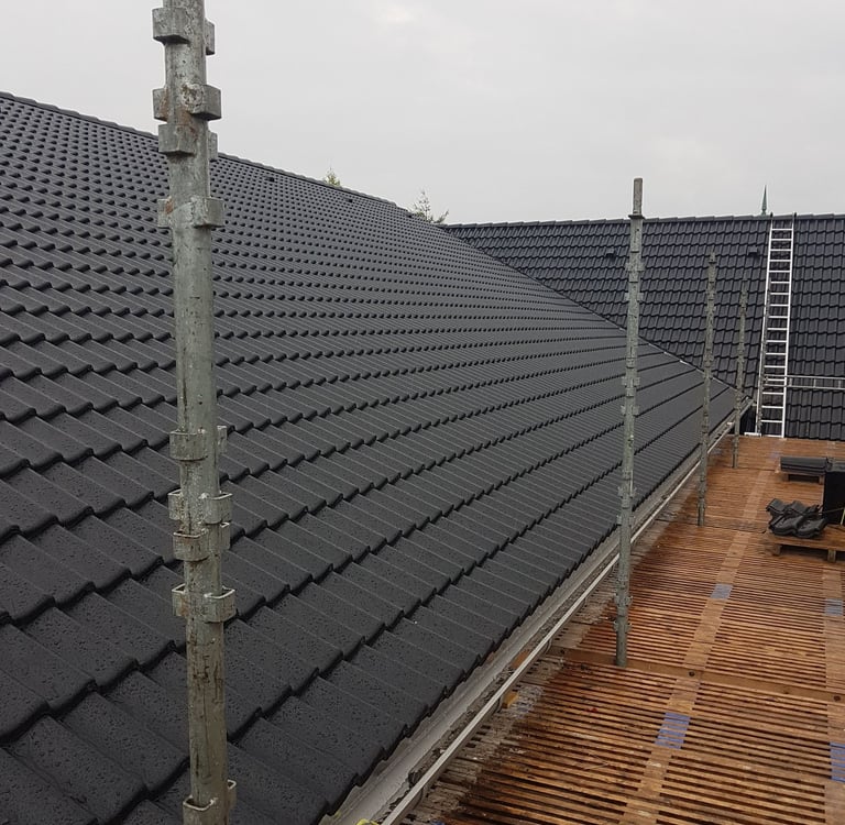 Professionel montering af sorte tagsten på et beboelseshus med sikkerhedsstillads.