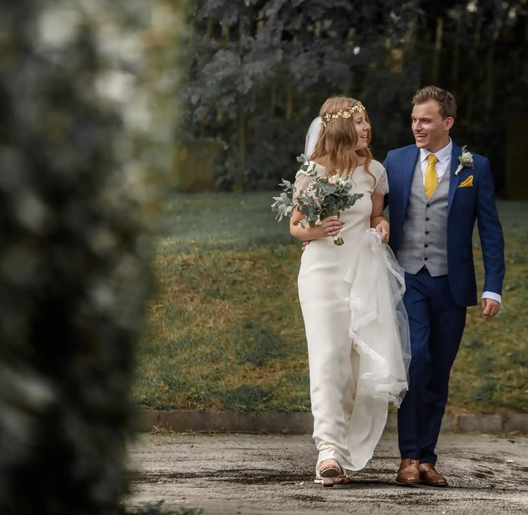 A smiling bride and groom walking together outdoors after their wedding ceremony.