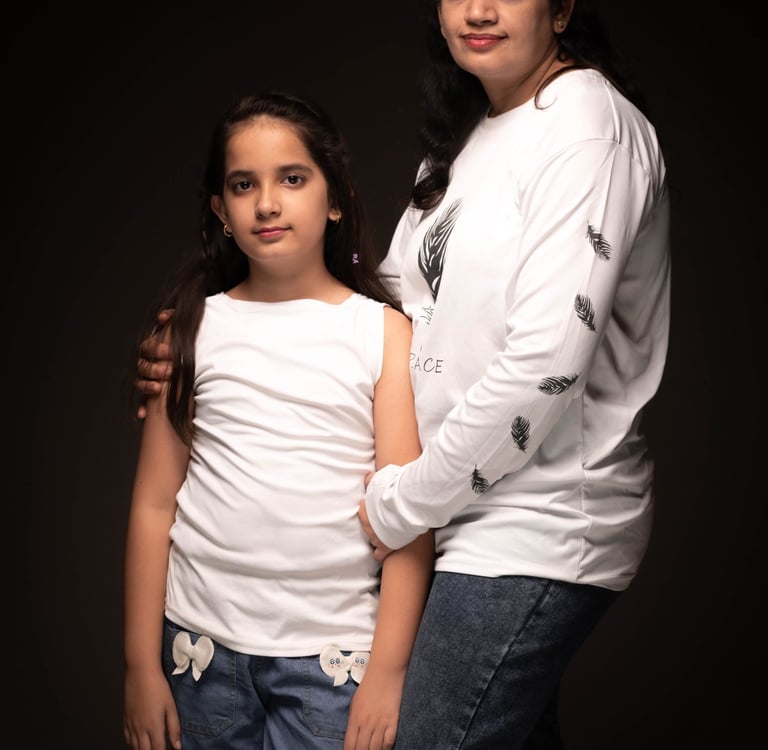 A portrait of a mother and daughter posing together in white shirts and denim jeans against a dark background.