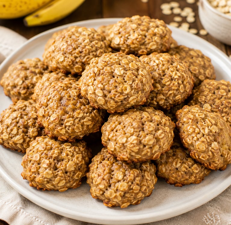 A plate of homemade soft oatmeal banana cookies on a rustic table with fresh fruit.