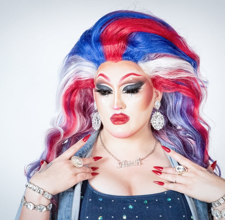 elagant headshot of drag queen pensively looking down with a large red, white, and blue wig
