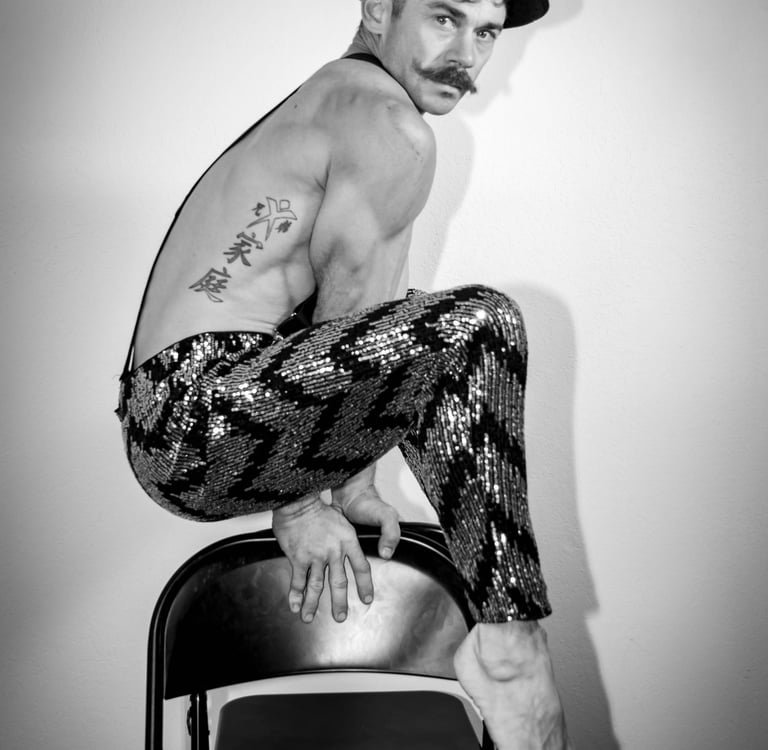 Black and white portrait of muscular circus performer suspended over chairs with shiny pants