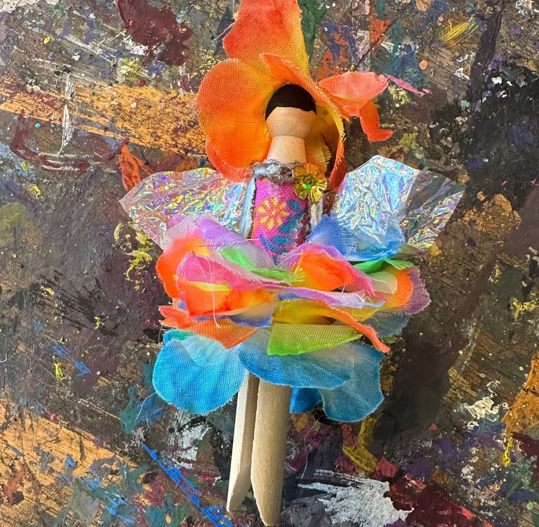 flower fairy clothespin doll laying on a paint-splattered table