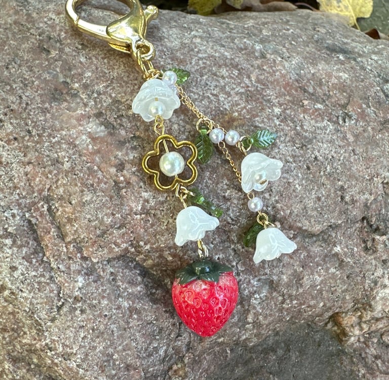 strawberry and flowers key chain with gold tone metal clasp and chain, laying on a rock