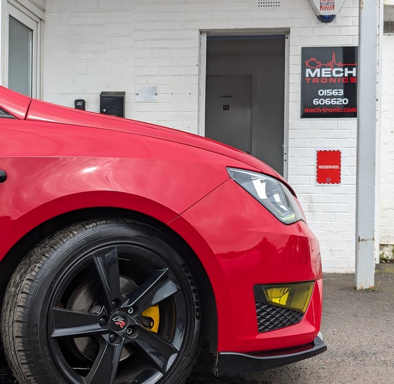 Red Seat Ibiza with black alloy wheels parked outside a Mech Tronics automotive repair shop.