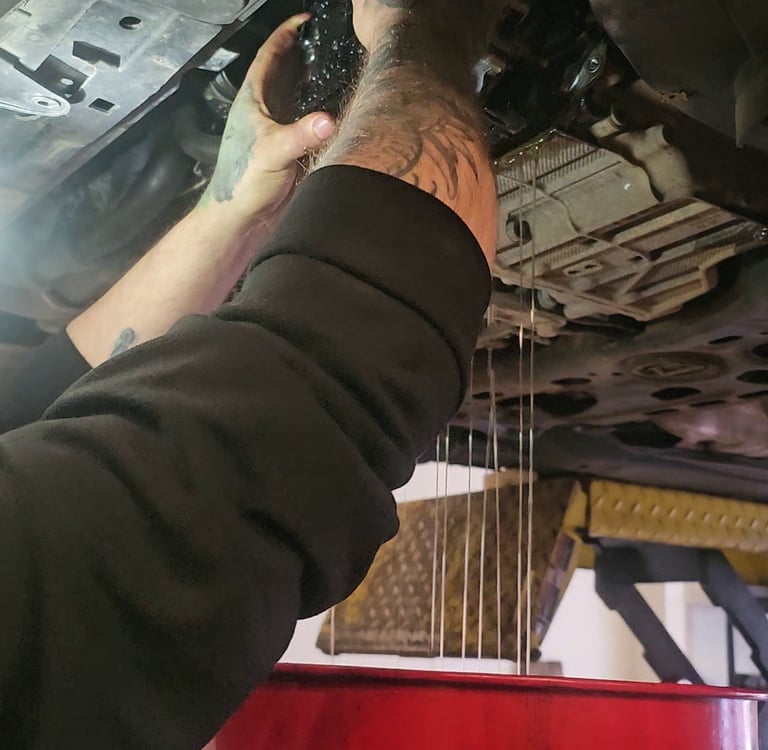 A mechanic draining old oil into a red collection pan during a mechatronic repair