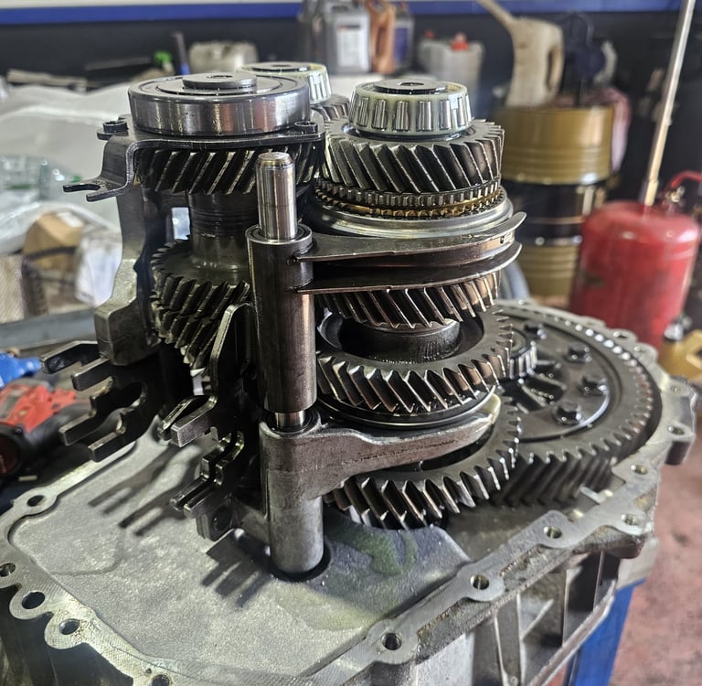 Manual car transmission gears and internals being repaired in an automotive workshop.