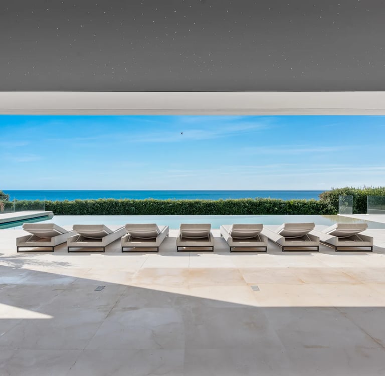 Luxury poolside patio with lounge chairs overlooking a modern infinity pool and the blue ocean.