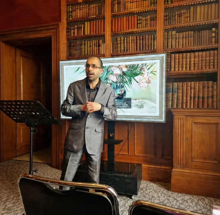 Professional speaker in a grey suit giving a presentation in a classic library with wood bookshelves.