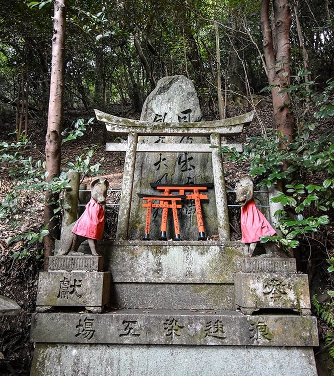 Petit sanctuaire dans la montagne avec des mini portes torii et deux kami renards sur les cotés