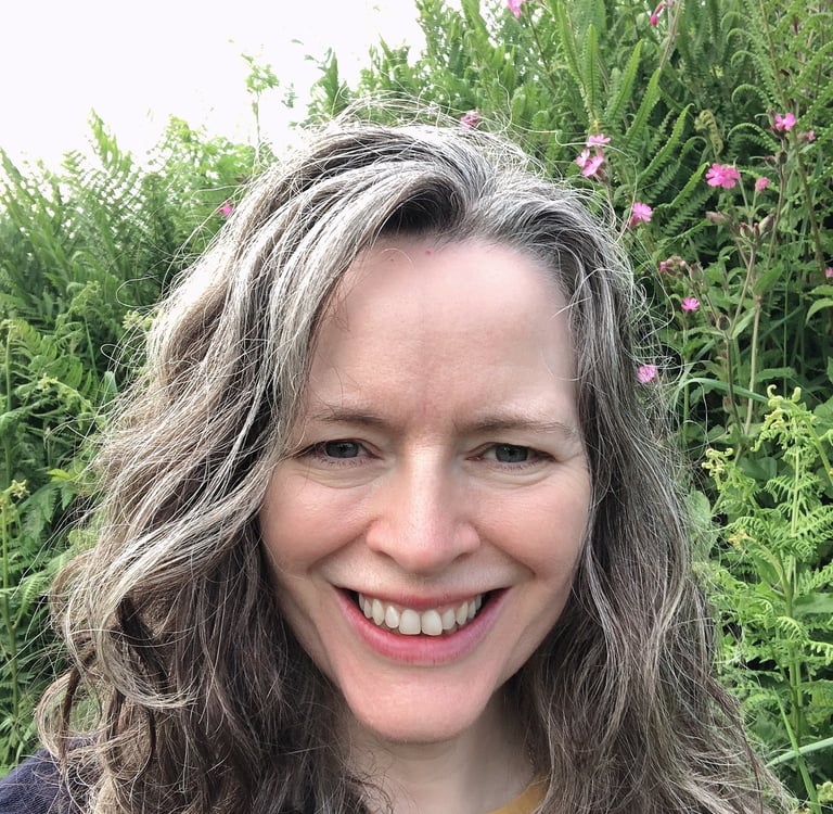 smiling woman with greying hair standing before wild flowers