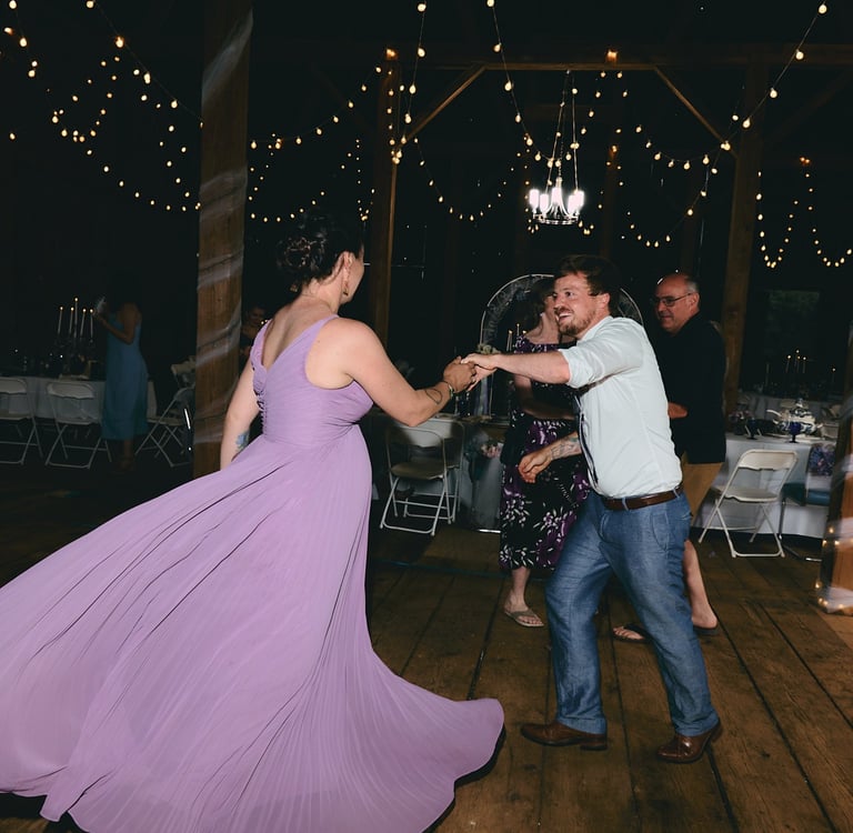 a man and woman in a purple dress dancing at a wedding reception in a barn