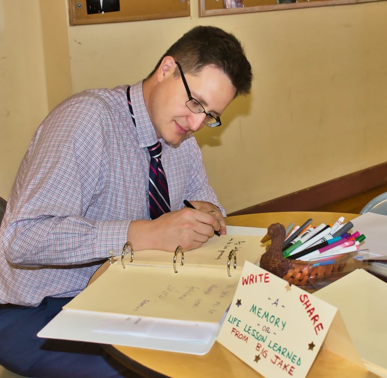 a man sitting at a table writing on a notepad