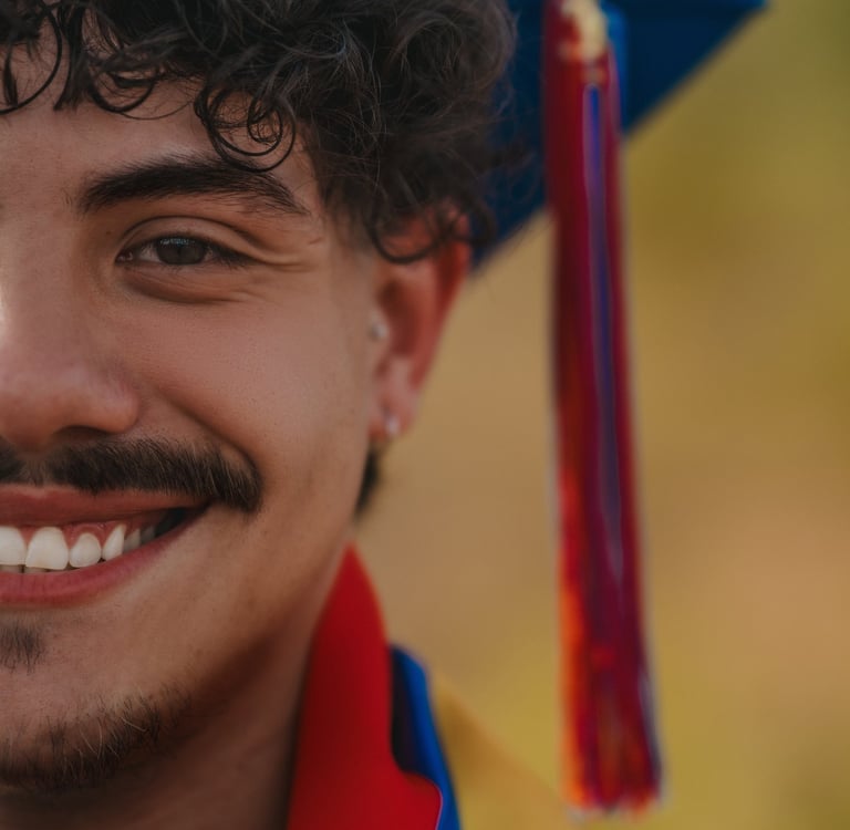A smiling male graduate with curly hair wearing a blue graduation cap and colorful tassel.