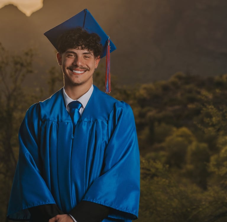 Smiling male graduate in blue cap and gown during a desert sunset graduation photoshoot.