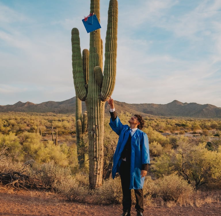 A college graduate in a blue gown tosses his cap onto a tall saguaro cactus in the Arizona desert.