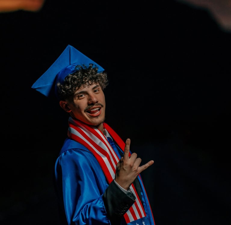 Smiling male graduate in blue cap and gown wearing a US flag stole during a sunset portrait.