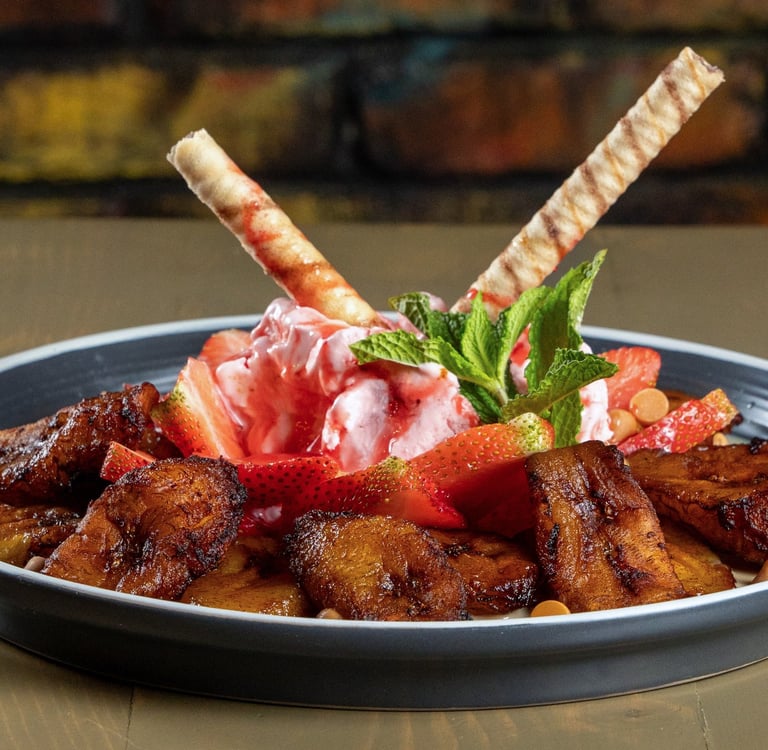 Postre de plátanos fritos con fresas, helado de fresa, barquillos y hojas de menta.