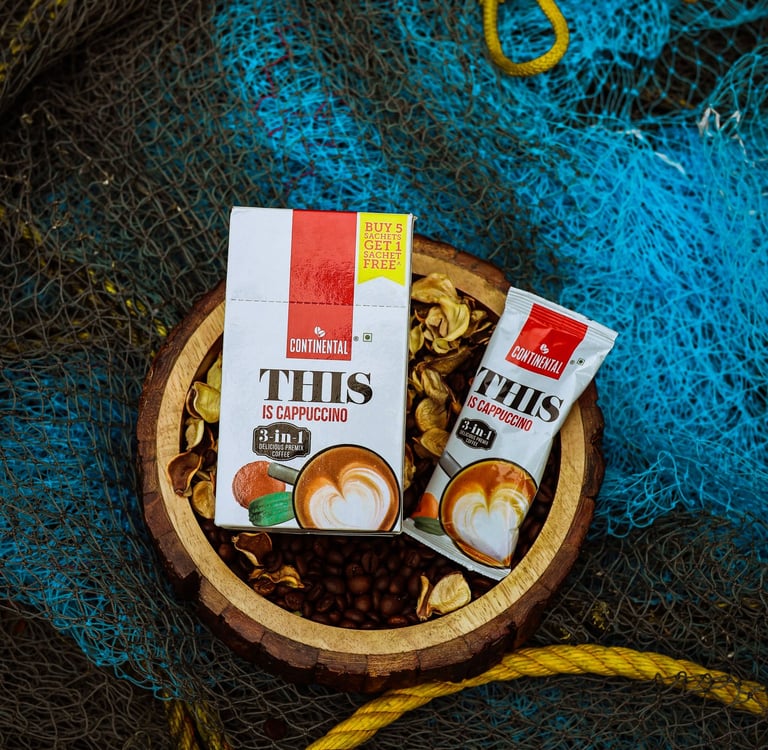 Continental This Is Cappuccino 3-in-1 instant coffee premix box and sachet on a rustic wooden bowl.