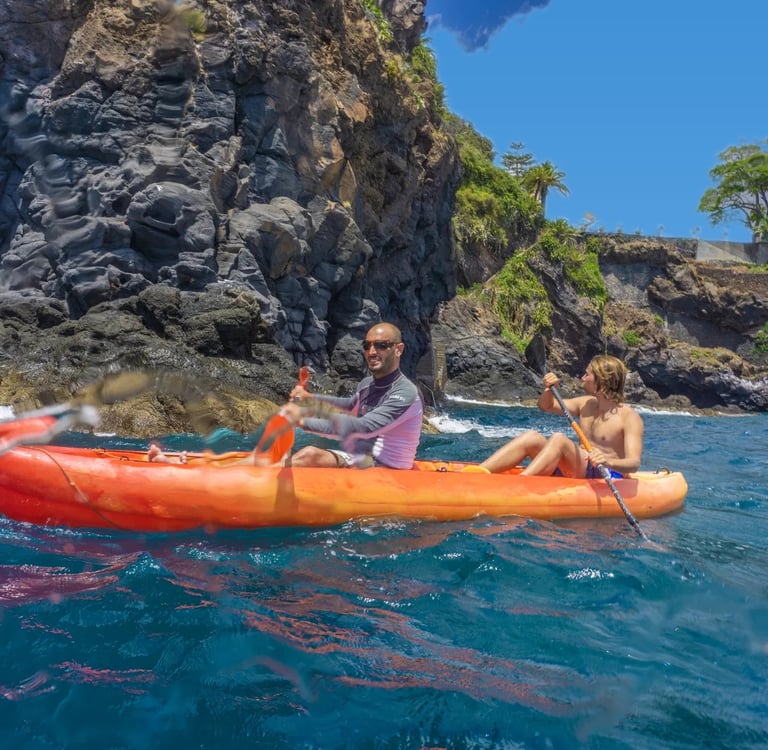 Guide and guest paddling an orange tandem kayak along the rocky volcanic cliffs of Funchal, Madeira