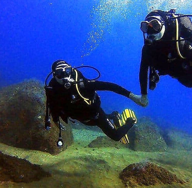 Two scuba divers exploring the underwater rocky seabed during an ocean dive in Funchal, Madeira