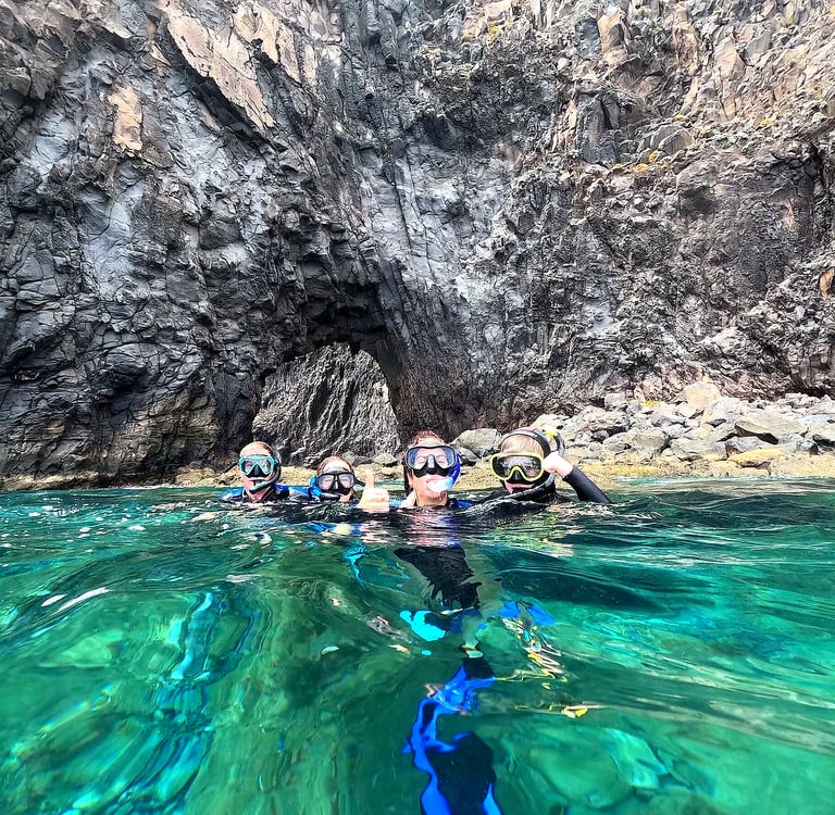 Group of snorkelers in green water in front of a volcanic rock arch at Ponta de São Lourenço, Madeira