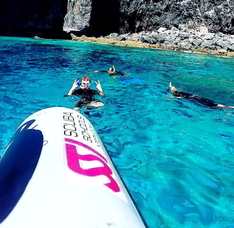 Snorkelers in crystal clear turquoise water next to volcanic rocky cliffs at Ponta de São Lourenço, Madeira